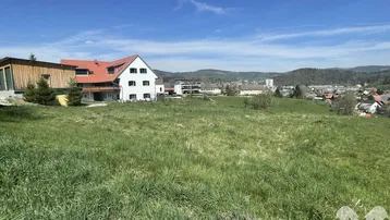 Weitläufiges Grundstück mit Blick auf umliegende Häuser und grüne Hügel unter blauem Himmel.