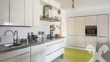 Moderne Küche mit weißen Schränken, integriertem Backofen und einer Arbeitsplatte in Betonoptik.