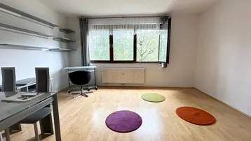 Heller Wohn- und Essbereich mit Parkettboden, großem Fenster und praktischen Wandregalen.