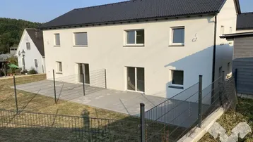 Rückseite der Doppelhaushälfte mit großer gepflasterter Terrasse und angrenzendem Garten.
