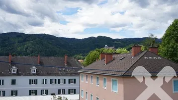 Weitläufiger Blick über Dächer und grüne Hügel, mit bewölktem Himmel und Fernsicht.