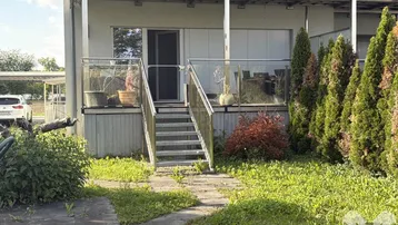 Terrasse mit Glasgeländer und Treppe, die zum grünen Gartenbereich des Hauses führt.