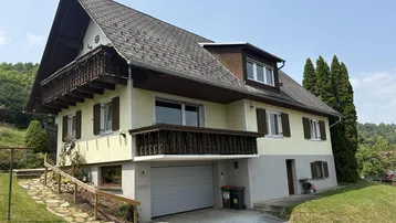 Traditionelles Einfamilienhaus mit Satteldach, Balkonen und integrierter Garage in ländlicher Umgebung.