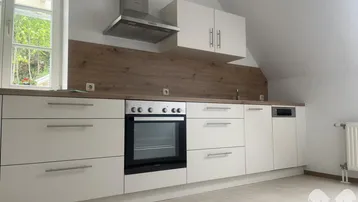 Moderne Einbauküche im Dachgeschoss mit weißen Schränken, Holzoptik-Arbeitsplatte und Fenster.