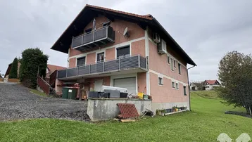 Rosa verputztes Haus mit mehreren Balkonen und angrenzender Grünfläche unter bewölktem Himmel.