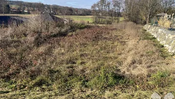 Unbebautes Grundstück mit Blick auf die umliegende Landschaft und entfernte Häuser unter blauem Himmel.
