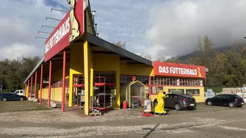 Großes Geschäftsgebäude mit gelber Fassade und rotem Dach, umgeben von einem Parkplatz und Bäumen.