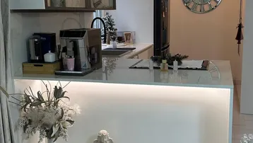 Moderne Küche mit heller Arbeitsplatte, integrierter Beleuchtung und großem Wanduhr als Dekoration.