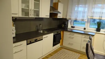 Moderne Küche mit weißen Schränken, dunkler Arbeitsplatte und Fenster mit Blick ins Grüne.