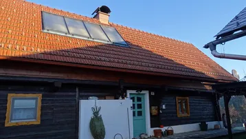 Vorderansicht des Holzhauses mit Ziegeldach, Solaranlage und hellblauer Eingangstür.