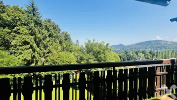 Panoramablick von einem Balkon auf die umliegenden Berge und grüne Wälder.