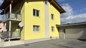 Gelbes Einfamilienhaus mit Balkonen, Garage und gepflasterter Auffahrt unter blauem Himmel.