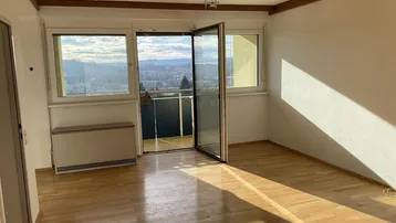 Helles Wohnzimmer mit Holzbalkendecke, Parkettboden und Zugang zu einem Balkon mit Weitblick.