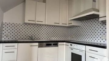 Helle Einbauküche mit weißen Schränken, dunkler Arbeitsplatte und gemustertem Fliesenspiegel.
