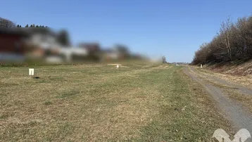 Offenes Feld mit einem Feldweg und Blick auf die umliegende Landschaft unter blauem Himmel.