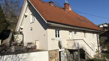 Ländliches Haus mit rotem Ziegeldach und Hanglage, umgeben von Natur.