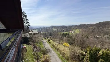 Panoramablick von einem Balkon über eine Straße, bewaldete Hügel und eine weite Landschaft.