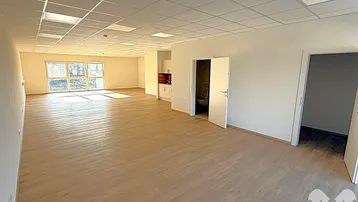 Großer, heller Büroraum mit modernem Laminatboden, vielen Fenstern und integrierter Küchenzeile.