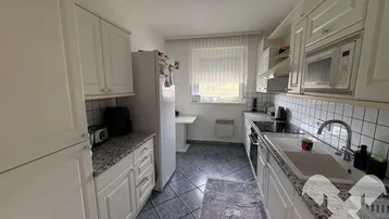 Helle Küche mit weißen Schränken, Granitarbeitsplatten und Fliesenboden mit Fenster.