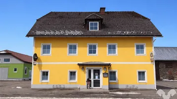 Gelbes Gebäude mit traditioneller Architektur, dunklem Ziegeldach und weißen Fenstern unter blauem Himmel, mit Fahrradständern davor.
