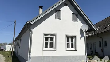 Weiß verputztes Einfamilienhaus mit Satteldach und kleinen Fenstern unter blauem Himmel.