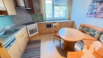 Gemütliche Küche mit Essbereich, Holzschränken und Blick ins Grüne durch das Fenster.