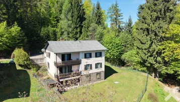 Hausfassade mit mehreren Balkonen und umgeben von üppiger Natur und Wald.