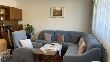 Gemütliches Wohnzimmer mit Ecksofa, Teppichboden und Holzmöbeln, ideal zum Entspannen.