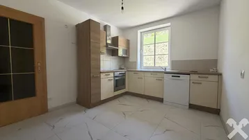 Moderne Einbauküche mit hellen Fronten, Fliesenboden und Fenster mit Grünblick.