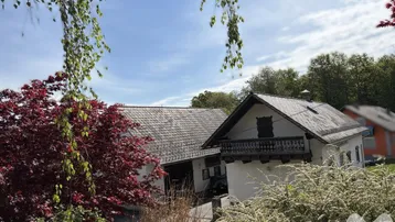 Ansicht des Hauses mit traditionellem Balkon und üppiger Frühlingsbepflanzung im Vordergrund.