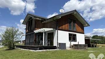 Modernes Einfamilienhaus mit Holzfassade, weißem Putz und einer einladenden Holzterrasse.