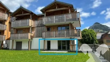 Modernes Gebäude mit Holzfassade, Balkonen und einer Terrasse mit Bergblick und Grünfläche.