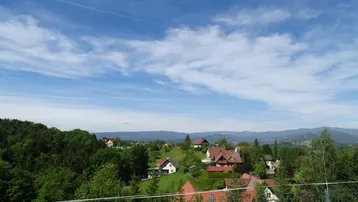 Weitläufiger Blick über die grüne Landschaft mit verstreuten Häusern und Bergen im Hintergrund.