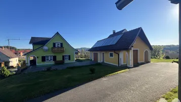 Weitläufige Ansicht zweier traditioneller Häuser mit grüner und gelber Fassade, umgeben von ländlicher Landschaft und Solaranlage.
