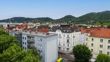 Panoramablick über die Stadt mit Wohngebäuden und grünen Hügeln im Hintergrund.