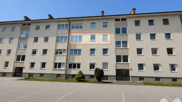 Mehrfamilienhaus mit mehreren Etagen und Parkplätzen im Vordergrund, die Wohnung ist rot markiert.