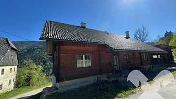 Traditionelles Holzhaus in alpiner Umgebung unter strahlendem Sonnenschein mit Blick auf die Berge.