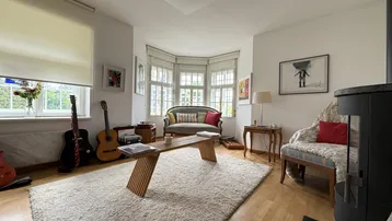 Gemütliches Wohnzimmer mit Holzboden, Erkerfenster, Sofa und einem modernen Holzofen.