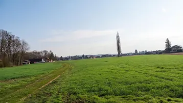 Weitläufiges grünes Feld mit Blick auf die umliegende Landschaft und Häuser in der Ferne unter blauem Himmel.