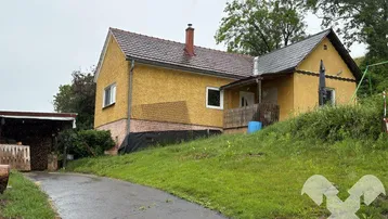 Gelbes Einfamilienhaus mit Satteldach und Zufahrt in ländlicher Umgebung.
