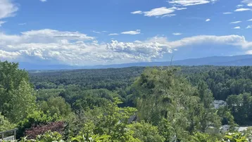 Weitläufiger Blick über grüne Wälder und Hügel unter einem blauen Himmel mit Wolken.
