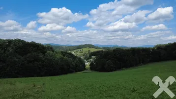 Weitläufige grüne Hügellandschaft unter blauem Himmel mit weißen Wolken und einem Dorf in der Ferne.