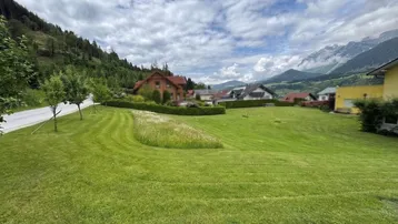 Weitläufige grüne Wiesenlandschaft mit Blick auf die umliegenden Berge und Wohnhäuser.