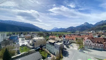 Weitläufiger Blick über die Stadt und die umliegende Berglandschaft unter einem bewölkten Himmel.