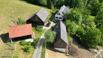 Luftaufnahme eines ländlichen Anwesens mit mehreren Gebäuden und viel Grünfläche in hügeliger Landschaft.