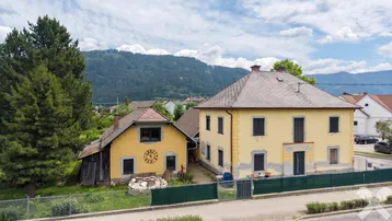 Zwei gelbe Häuser mit Satteldächern und einem Gartenbereich vor einer Bergkulisse.