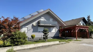 Ansicht des Einfamilienhauses mit Solarpaneelen auf dem Dach und gepflegtem Vorgarten.