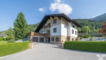 Großzügiges Einfamilienhaus im alpinen Stil mit Doppelgarage und gepflegter Auffahrt, umgeben von grüner Landschaft.