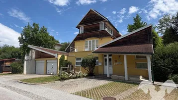 Gelbes Haus mit Holzverkleidung, Doppelgarage und gepflasterter Auffahrt unter blauem Himmel.