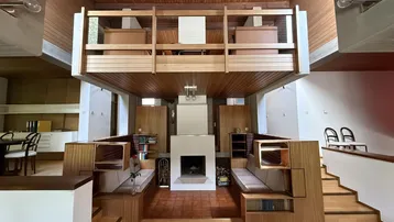 Geräumiges Wohnzimmer mit hoher Holzdecke, Kamin und offener Galerie, die zum Entspannen einlädt.